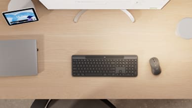Top view of Logitech Signature Slim Solar+ K980 keyboard, wireless mouse, laptop, tablet, and part of a screen on a work desk